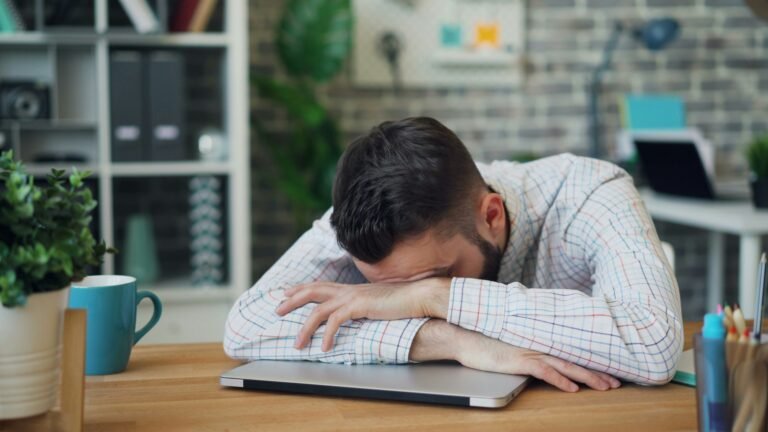 Portrait of young man employee sleeping on desk in office relaxing at work